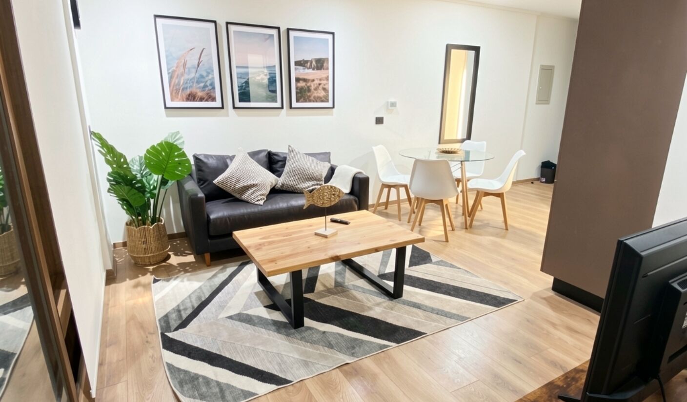 Una sala de estar con sofá, mesa de centro y sillas. Hay cuadros en la pared, una planta en maceta y un espejo.