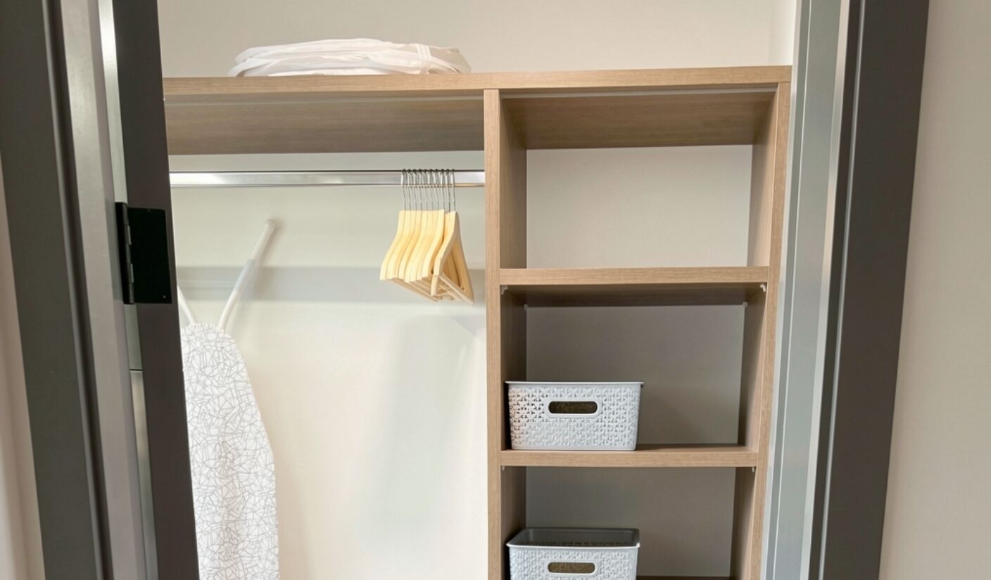 A closet with wooden shelves, hanging clothes, and storage boxes.