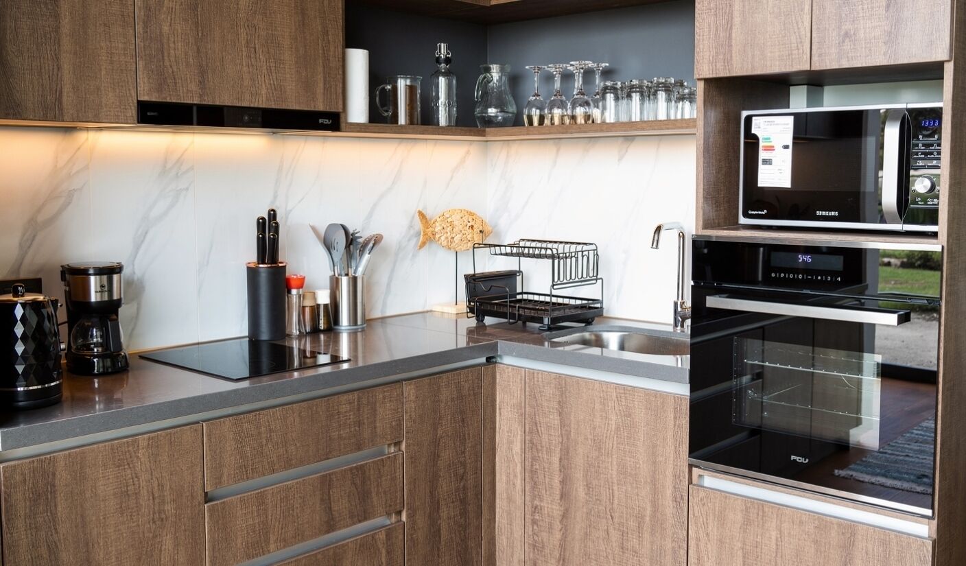 Una cocina moderna con armarios de madera, horno empotrado, microondas y cafetera.