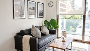A modern living room with a black leather sofa, two framed pictures, a large plant, and a wooden coffee table with a decorative object. - Corporate Stays Somma Asturias (Santiago)