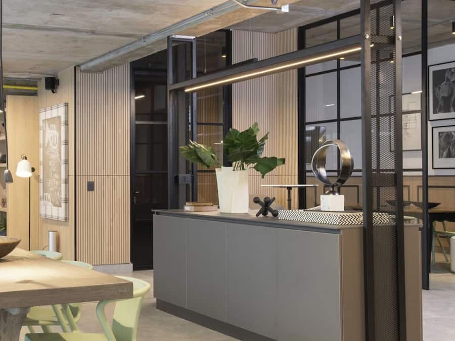 A modern kitchen with a long island, bar stools, pendant lighting, and a large window.