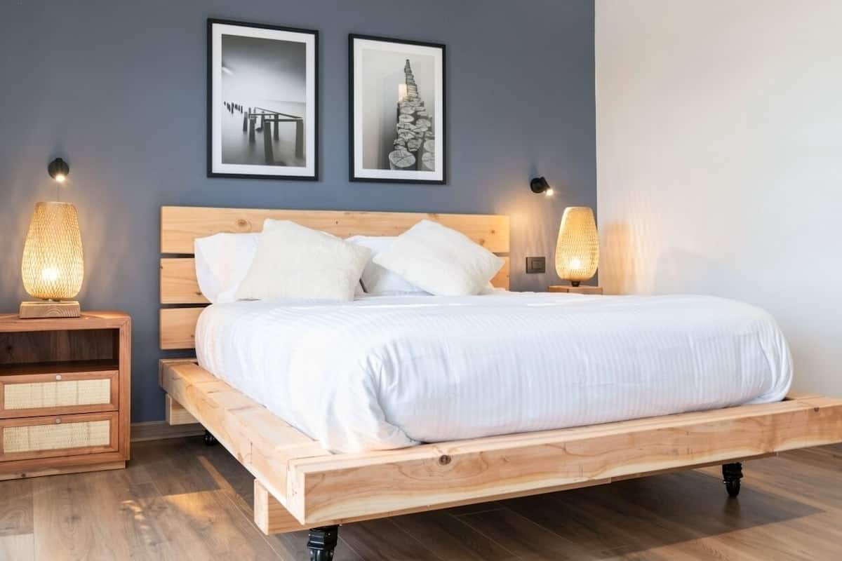 A modern bedroom with a wooden bed, two bedside tables with lamps, and two framed pictures on the wall.