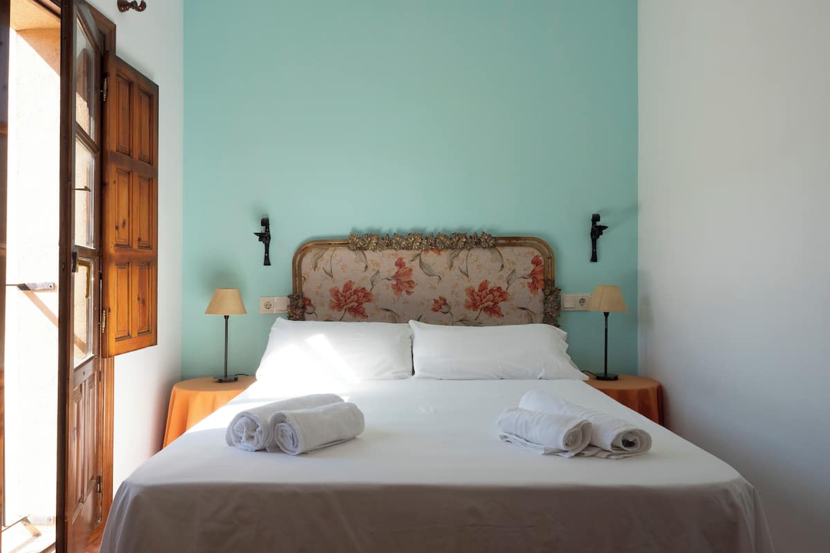 A neatly made bed with white linens and two rolled towels, a wooden door, and two bedside tables with lamps.