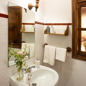 Casa de banho com lavatório branco, espelho, porta-toalhas e janela com vista.
