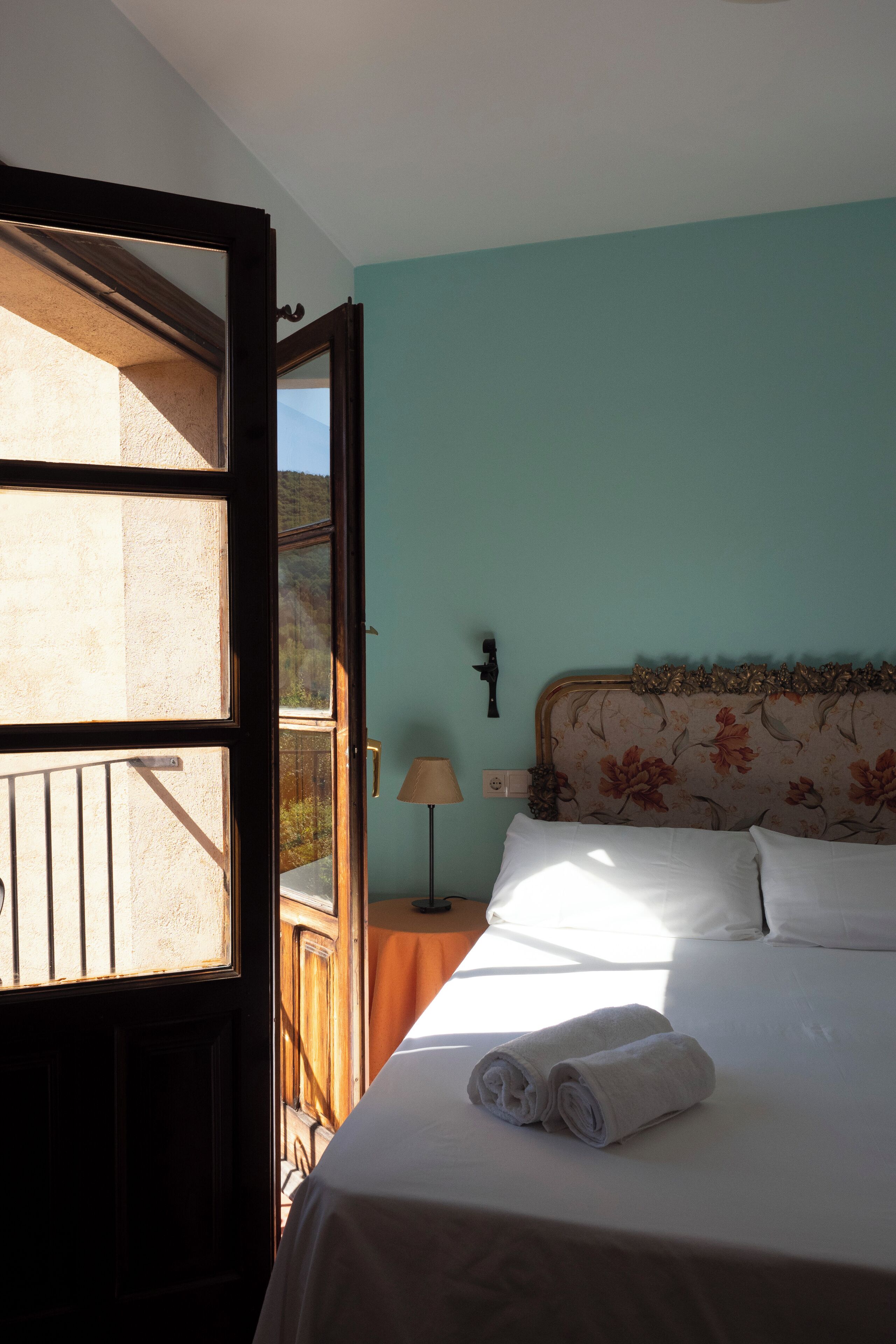 A bedroom with a bed, a nightstand, a lamp, and a view through an open door.