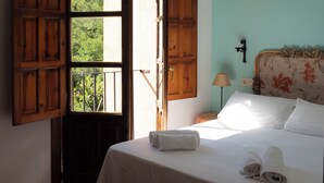 A bedroom with a bed, a nightstand, a lamp, and a window with open shutters. - hotel rural el jardin del conde (Peñacaballera)