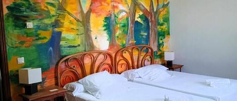 A room with two beds, a wooden headboard, and a colorful mural on the wall.