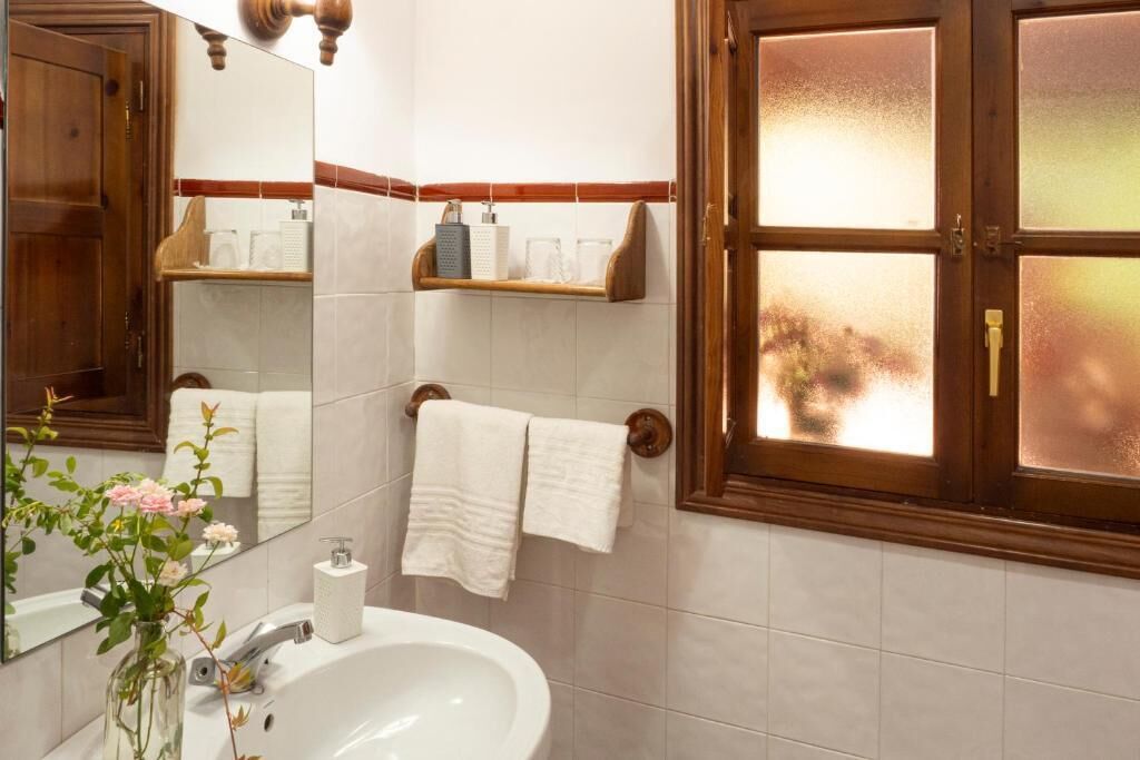 A bathroom with a white sink, a mirror, a window with frosted glass, and a towel rack.