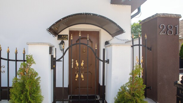 Una entrada protegida con una puerta marrón, un letrero encima de la puerta y el número '281' en una pared a la derecha.