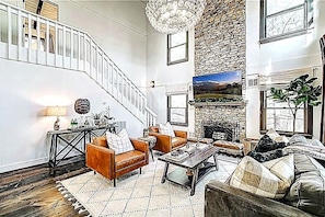 A living room with a staircase, a fireplace, and a large window.