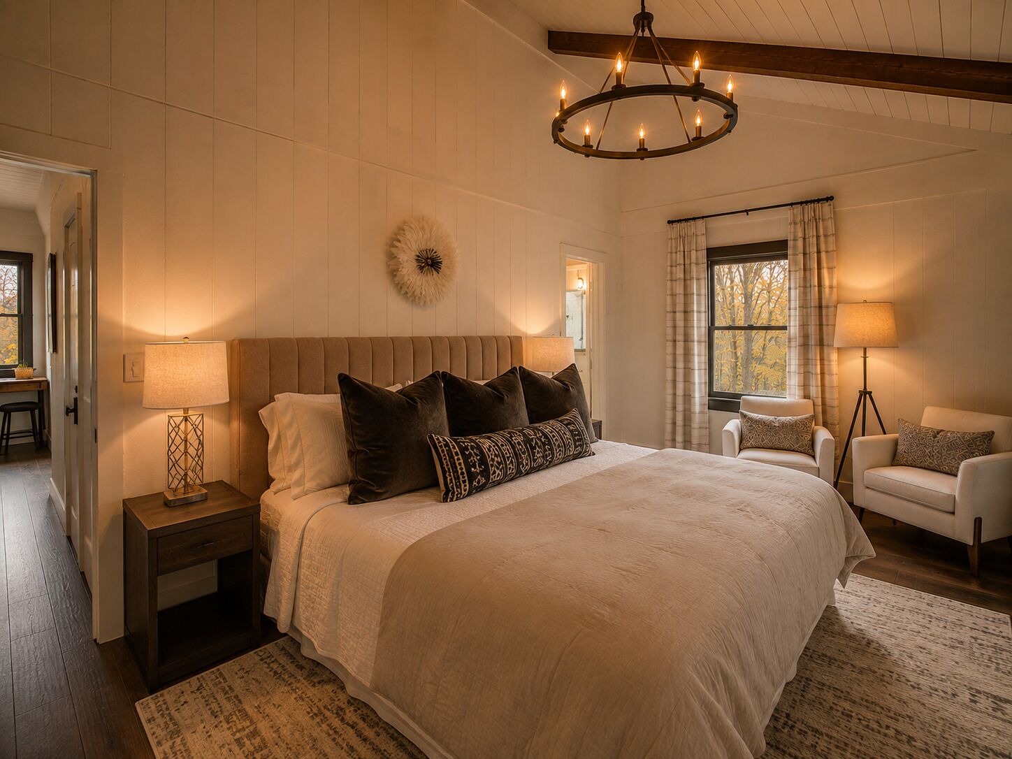 A bedroom with a large bed, bedside lamps, a chandelier, a window with curtains, and a chair.