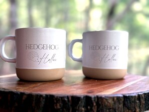 Two mugs with 'Hedgehog Hollow' embossed on them, placed on a wooden surface outdoors. - Luxury 3BR Retreat in Big Canoe-Hedgehog Hollow (Jasper)