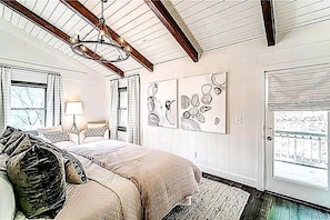 A bedroom with a bed, a chandelier, a door, and artwork on the wall.