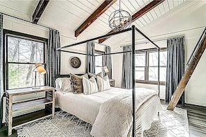 A bedroom with a four-poster bed, a window with curtains, a lamp on a nightstand, and a wooden ceiling beam. - Luxury 3BR Retreat in Big Canoe-Hedgehog Hollow (Jasper)