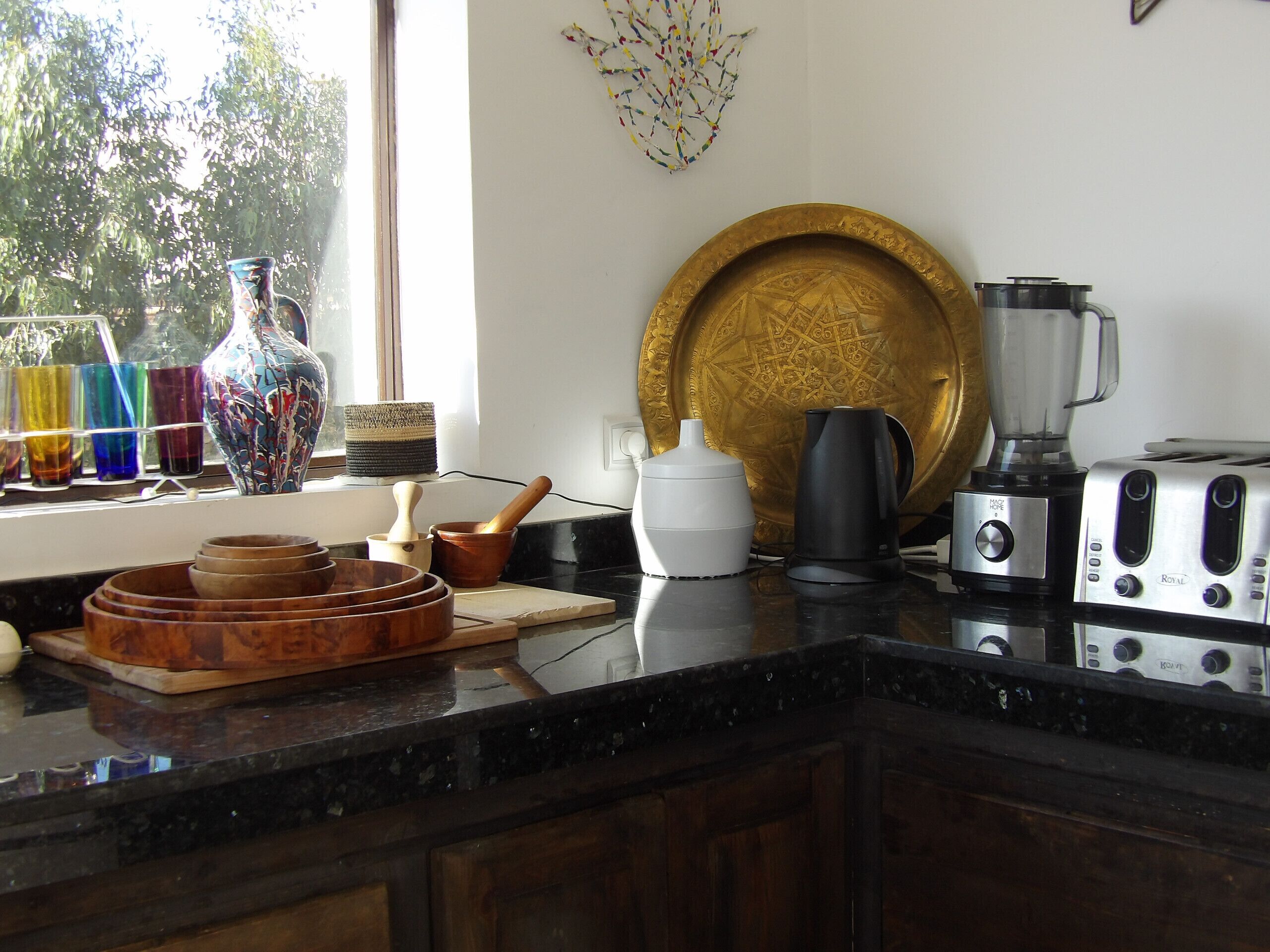 A kitchen with a window, a wooden cutting board, a coffee maker, a blender, and a toaster.