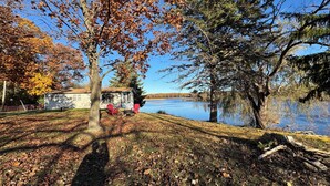 A cabin by a lake with a clear view of the water, surrounded by trees with autumn leaves. - Long Lake Retreat - Cottage in Burlington, WI (Burlington)