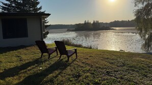 A lakeside view with two Adirondack chairs facing the water, a small cabin, and a clear sky. - Long Lake Retreat - Cottage in Burlington, WI (Burlington)