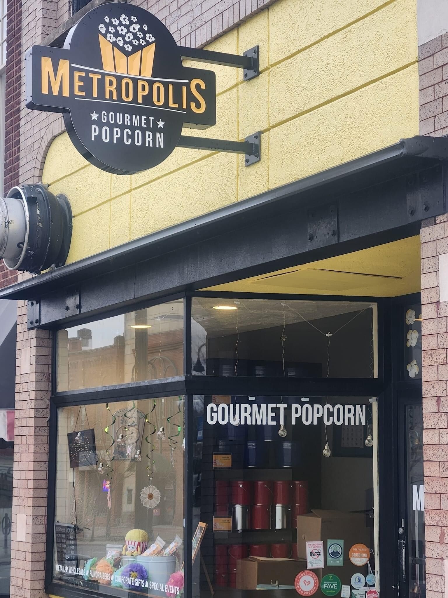 A storefront with a sign reading "METROPOLIS GOURMET POPCORN" and a window displaying various popcorn containers.