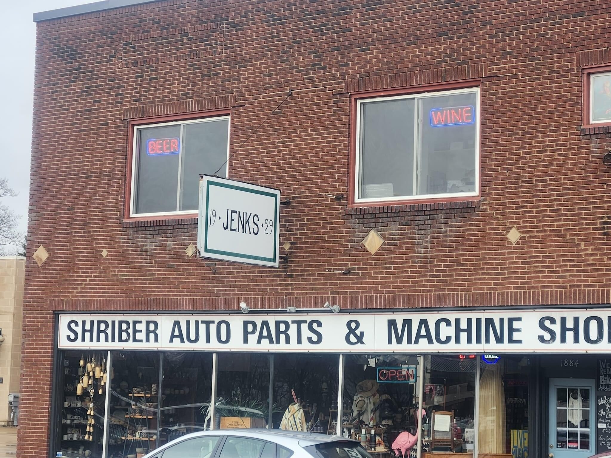 Un edificio de ladrillo con un letrero que dice 'Shriber Auto Parts & Machine Shop' y letreros de neón que anuncian 'Cerveza' y 'Vino'.