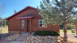 A small wooden cabin with a porch, a stone foundation, and a well-maintained garden. - Pine Creek Cabins - Cabin 2 (Pine)
