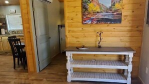 Interior de madeira com um banco, uma pintura de um cânion e uma área de cozinha ao fundo.