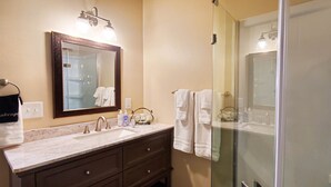 A bathroom with a large mirror, a sink with a marble countertop, a dark vanity, and a glass shower enclosure. - Pine Creek Cabins - Cabin 5 (L2) (Pine)