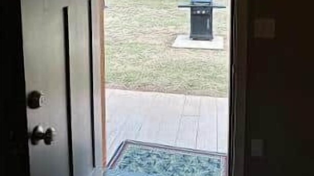 A doorway leading to a covered outdoor area with a bench and a trash can.