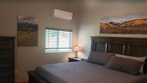 A bedroom with a large bed, a nightstand with a lamp, a dresser, and two landscape paintings on the walls. - Pine Creek Cabins - Cabin 1 (Pine)