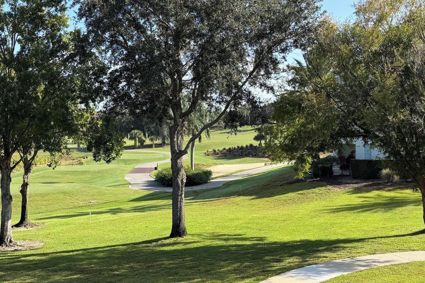 Un parcours de golf avec un chemin dégagé, des arbres et un bâtiment en arrière-plan.