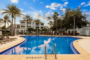 A swimming pool with a 5ft 6in depth, surrounded by lounge chairs and palm trees, with a multi-story building in the background.