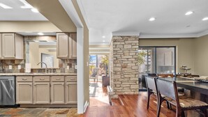 A modern kitchen with beige cabinets, a stone accent wall, and a dining area with a wooden table and chairs. - Lakeway Hill Country Home | Grill Deck, Tennis Courts + Trails (Lakeway)