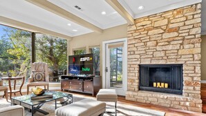 A modern living room with a stone fireplace, a glass coffee table, and a comfortable seating area. - Lakeway Hill Country Home | Grill Deck, Tennis Courts + Trails (Lakeway)