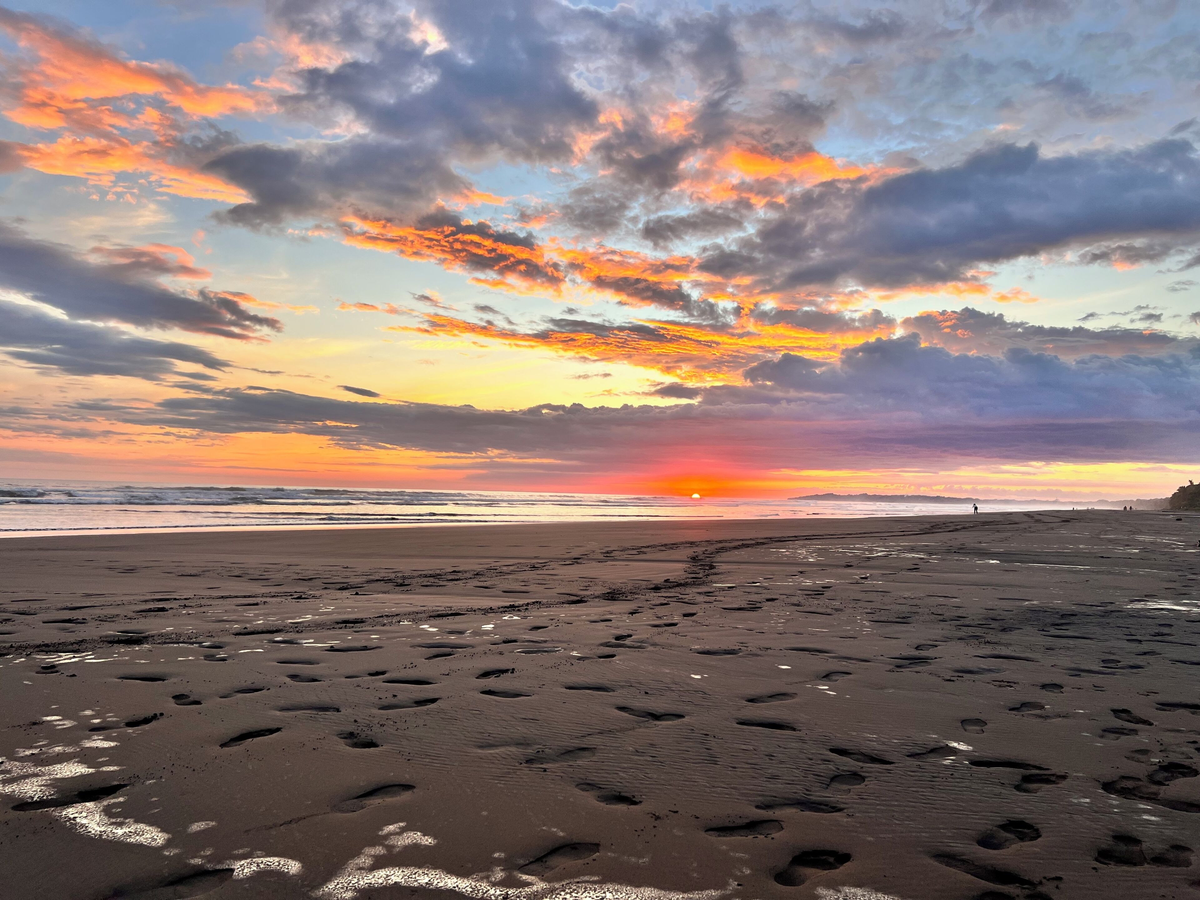 A beach with footprints and a sunset in the background.