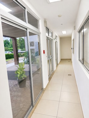 A corridor with glass doors leading to an outdoor area, a tiled floor, and a ceiling with recessed lighting.