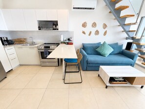 A modern kitchen with white cabinets, a microwave, and an oven. There is a dining table with a chair, a blue sofa, and a small wooden table. - 5th-Floor Oceanfront Penthouse, 3BR w Loft, Bejuco Beach - Playa Pura Vida (Bejuco)
