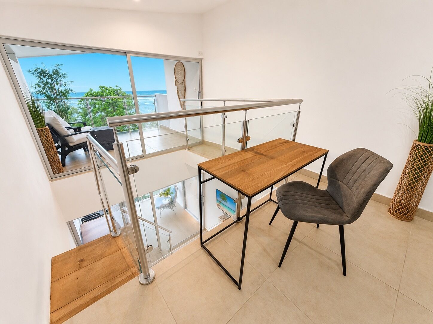 A modern interior with a wooden table and a chair, a glass railing, and a view of the outdoors.
