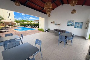 Un área de patio exterior con piscina, sillas de descanso y comedor.