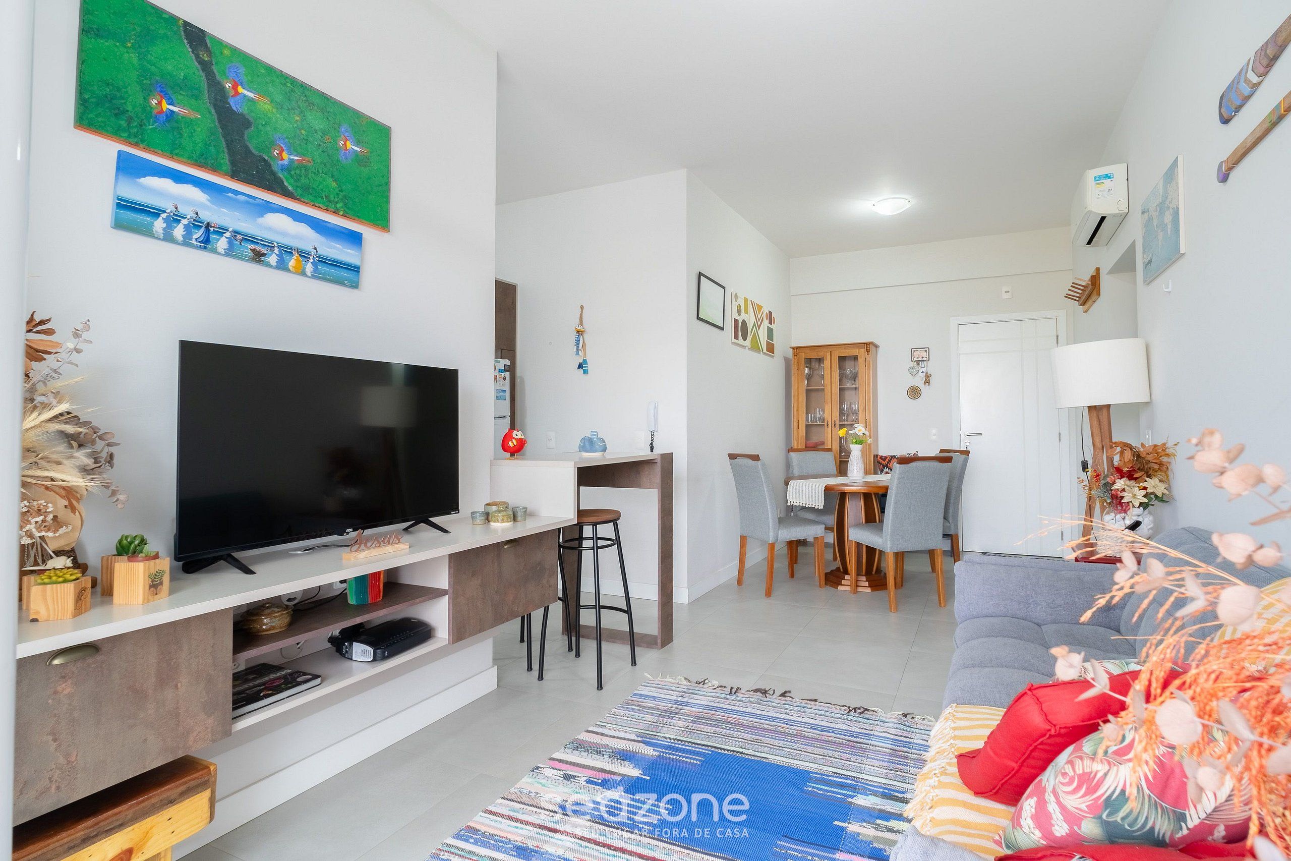 A modern living room with a flat-screen TV, a dining area with a wooden table and chairs, and a grey sofa.