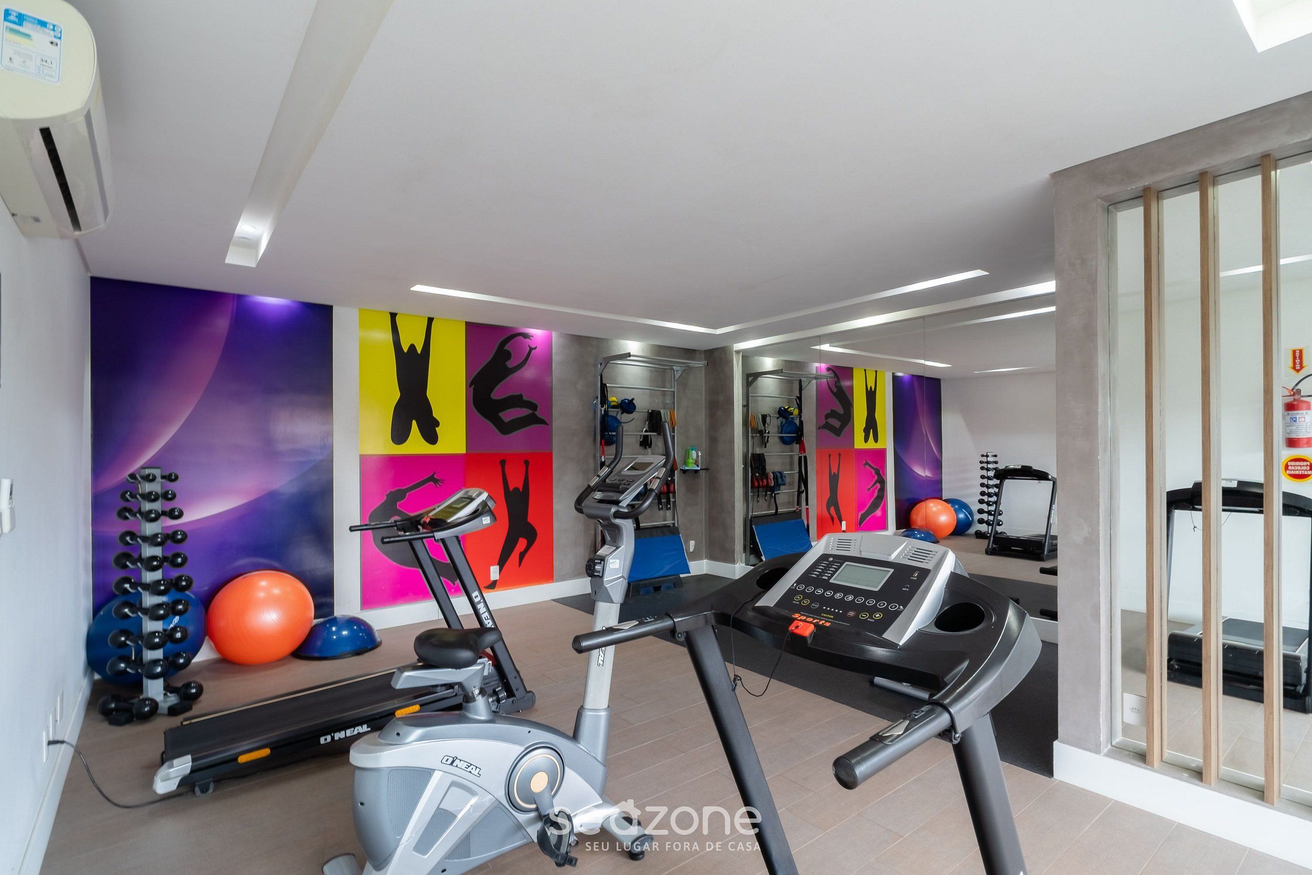 Un gimnasio con equipamiento de ejercicio, una cinta de correr y un espejo grande.