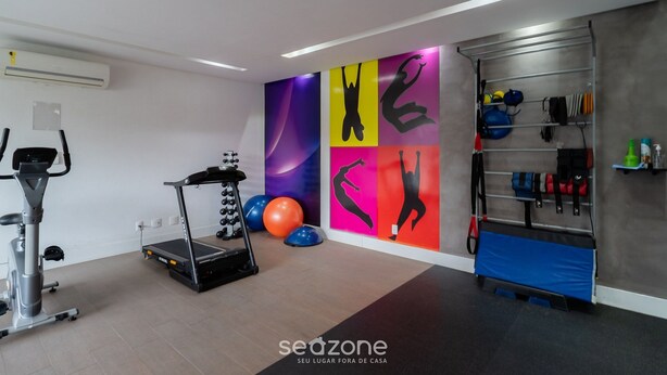 Een sportschool met trainingsapparatuur, een muur met kleurrijke silhouetten en een rek met diverse spullen.