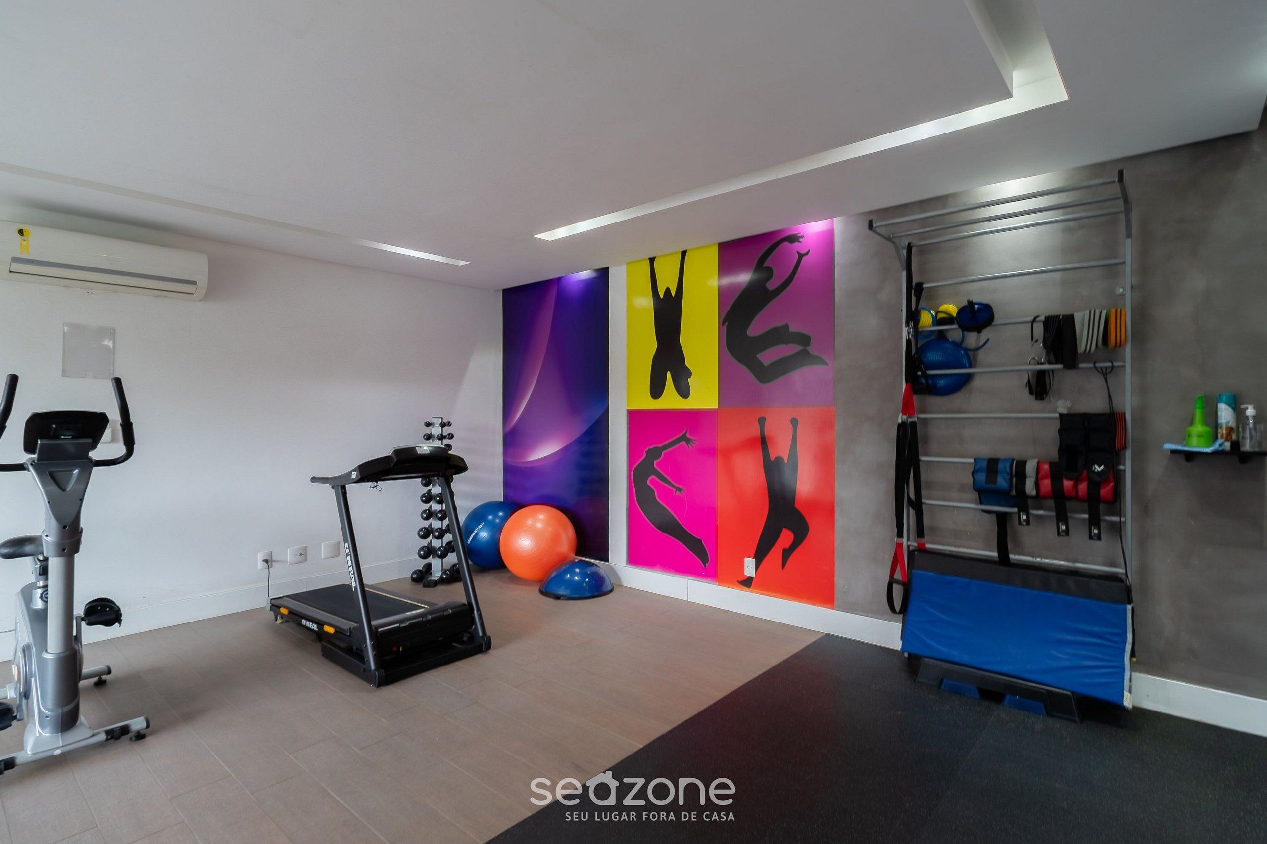 Un gimnasio con equipo de ejercicio, una pared con siluetas coloridas y un estante con diversos artículos.