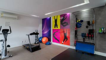 Un gimnasio con equipo de ejercicio, una pared con siluetas coloridas y un estante con diversos artículos.