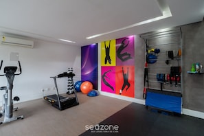 A gym with exercise equipment, a wall with colorful silhouettes, and a rack with various items. - Apart w/ Barbecue in Campeche Clc0104 (Florianópolis)