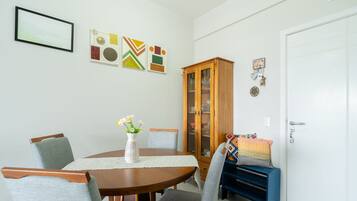 Un comedor con una mesa redonda de madera, cuatro sillas grises tapizadas, un jarrón blanco con flores y un aparador con puertas de cristal.
