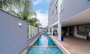 Un bâtiment moderne doté d’une piscine, de grandes fenêtres et d’espaces extérieurs aménagés pour se détendre.