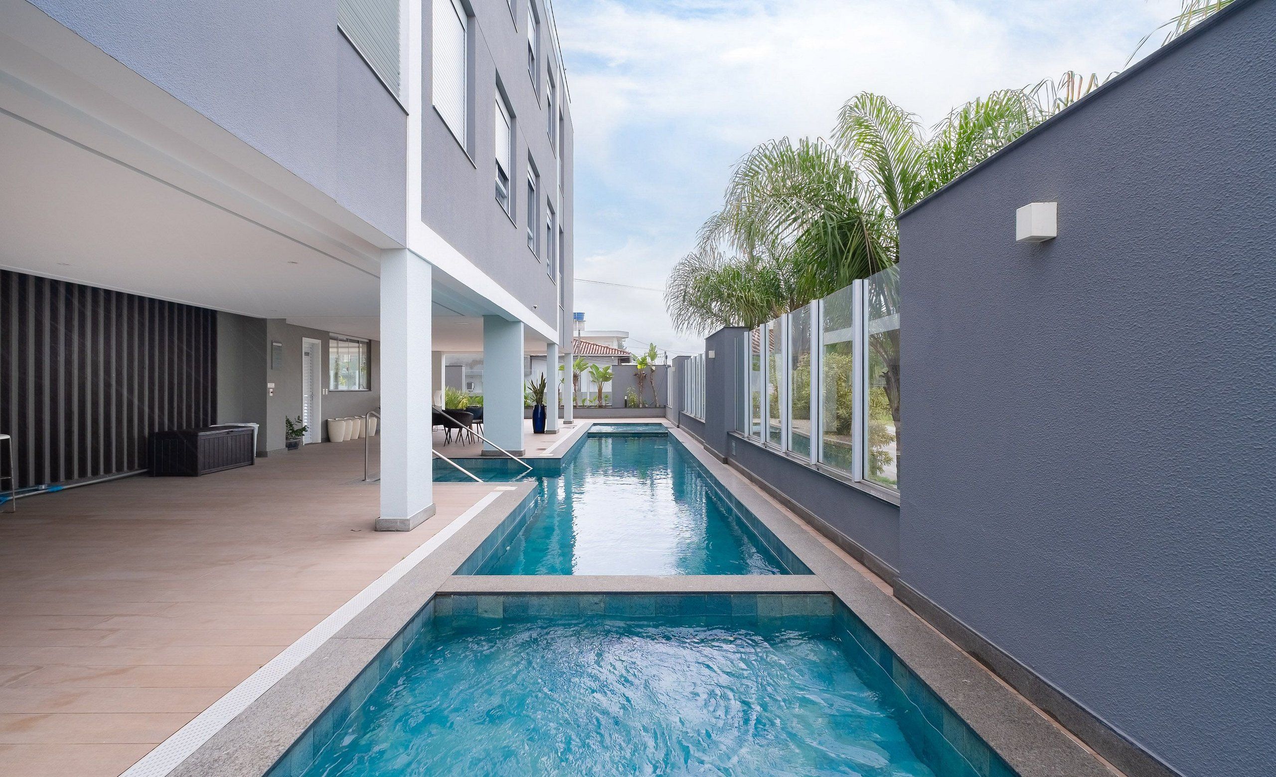 Ein moderner, überdachter Schwimmbereich mit freiem Blick auf die umliegende Architektur, darunter ein Gebäude mit großen Fenstern und einer grauen Außenwand.