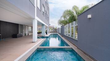 A modern indoor swimming pool with a clear view of the surrounding architecture, including a building with large windows and a grey exterior wall.