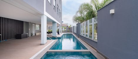 A modern indoor swimming pool with a clear view of the surrounding architecture, including a building with large windows and a grey exterior wall.