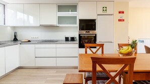Moderni keittiö, jossa on valkoiset kaapit, sisäänrakennettu uuni sekä ruokailutila, jossa on puinen pöytä ja tuolit.