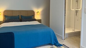 A modern hotel room with a large bed, a glass shower enclosure, and a nightstand with a lamp. - Quiet studio in a green setting (Charbonnières-les-Bains)